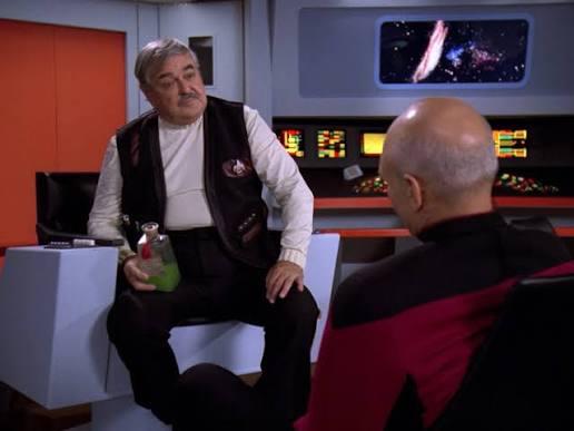 Scotty in a hologram of the original Enterprise and sitting in the captain’s chair talking to Picard who is faced away from the camera