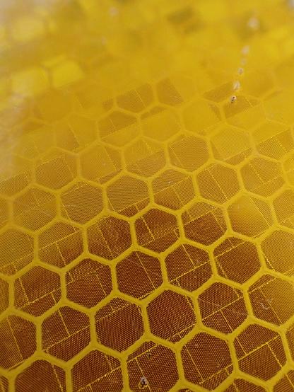 Macro closeup of a yield sign showing the reflective pattern. It kinda looks like a bee hive because of the yellow colors and prominent hexagon patterns. However, below the hexagon pattern is a pattern of tiled squares, and on each of the little squares are hundreds of little dots. There are a couple of blemishes.