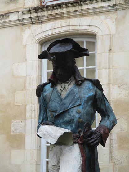 Buste de la statue où Toussaint Louverture en bicorne lit la Déclaration universelle des droits de l'homme et du citoyen, sa main droite posée sur son sabre sur son flanc gauche