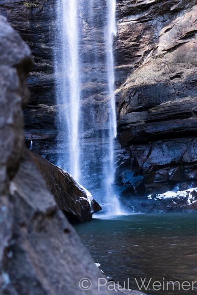 A vertical waterfall with some out of focus rock in the foreground