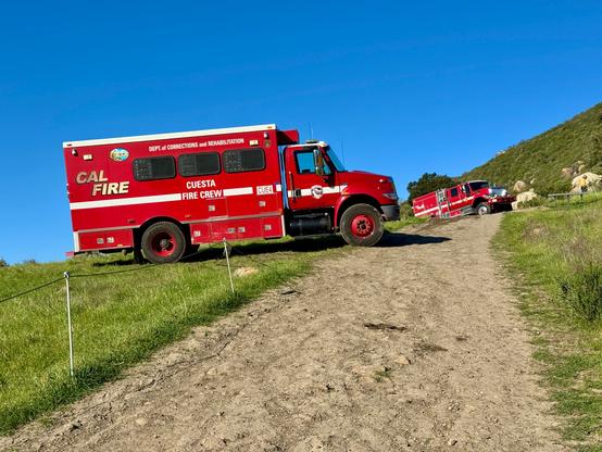 Two red CalFire trucks are parked on green grass at the side of a steep, wide trail going up Cerro San Luis under a bright blue sky. There had been a small fire that involved heavy, dead debris, so they had an extensive mop-up to do. Fortunately, not much damage. I'm thankful they were able to get up close to the fire location; not all trails are as easily accessible. San Luis Obispo, California
