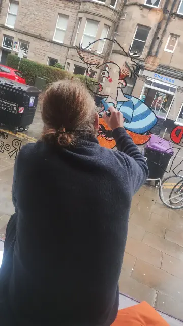 Looking over the shoulder of illustrator Ross Collins as he paints in the outline of one ofhis characters in the bookshop window