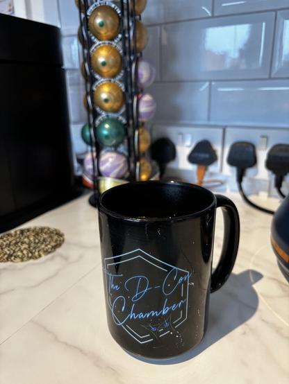 A black mug of tea that says The decon chamber on it.