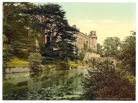 The image depicts a historic castle situated beside the River Avon in Warwick, England. The photograph is aged and has a sepia tone typical of early 20th-century printmaking processes known as photochroms. It features an impressive medieval stone structure with fortified towers and battlements along its walls. Surrounding trees frame the building, suggesting that it may be situated on elevated ground or within a park-like setting. The river is calm, reflecting parts of the castle's façade and vegetation from surrounding greenery. In terms of historical context, Warwick Castle has been occupied since Roman times; however, much of its current structure dates to medieval periods when such castles served as both residences for nobility and fortifications against invaders. This particular image likely originates around 1890-1900 based on the caption "Warwick The Castle."