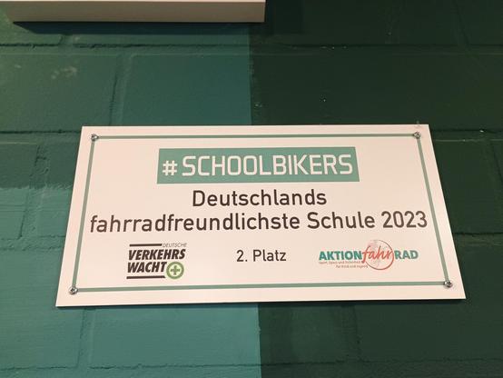 A foto of a sign at a green wall with mostly german text... #SCHOOLBIKERS - Germanys most bikefriendly school 2023 - 2nd place