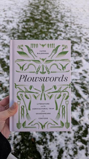 Holding the book "Plowswords" in front of a snowy meadow