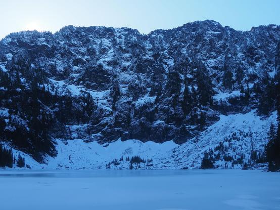 An ice-covered lake in a steep basin.  There is an avalanche fall at the far side of the lake.  The light is dark because the sun has just fallen behind the top ridge (it was not as cold as it looks though).  Lake 22 off the Mountain Loop Highway