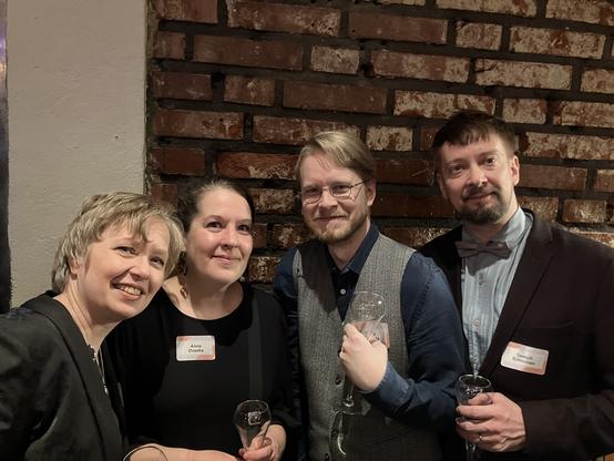 Four people with champagne glasses posing next to a red brick wall.