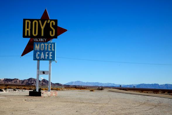 Roy's Motel and Cafe in Amboy California taken at midday.  Blue sky and mountain range in the distance.  Route 66 along the right of the frame.