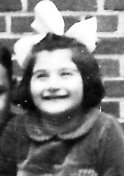 A vintage black and white photo of a smiling girl wearing a large bow on their head.