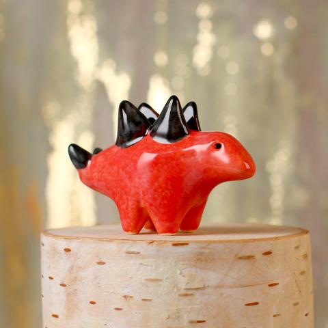 A small orange ceramic stegosaurus with black plates and thagomizer.