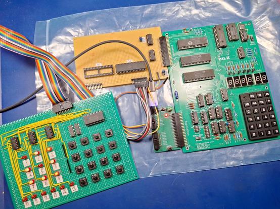A PAL-2 SBC with a homebrew VIA interface board, which looks half finished. A 6502 Gamesboard(tm) is attached to the VIA interface using a ribbon cable and a bunch of patch wires. Various LEDs on the Gamesboard are lit.