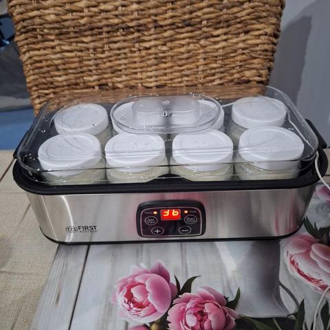 na stole jadalnym stoi niewielka jogurtownica z ośmioma słoiczkami pełnymi mleka.