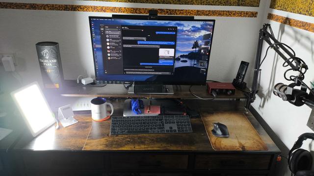 Man sieht einen Schreibtisch mit Computer, Monitor und Tastatur und Maus. Links steht eine leuchtende Tageslichtlampe.