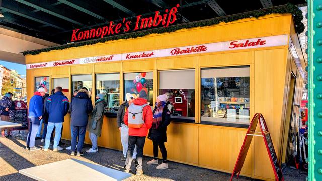 Colour photo of a currywurst food stall. Customers are placing orders at the window while others wait eagerly.
This establishment has been here since 1930.