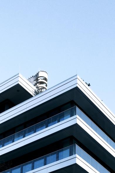 Photo up a layered building with inset balcony laced floors. Each level has an outset face of white bars. Ontop a series of round rings full of birds reaches towards the sky