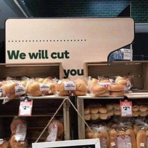 Display of packaged bread and buns in a store with a partially obscured sign that reads, "We will cut you..."