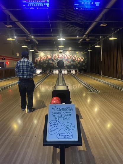 Neon lighted Bowling alley with a sign in between the lanes saying “Teachers should afford to live where they teach.” With money flying away and a thought bubble “why do cops get paid more than teachers. Asking for a friend.”