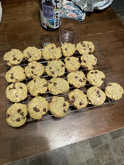 a photo of some chocolate & peanut butter chip cookies on a cooling rack on a wooden table with some drinkware in the background.