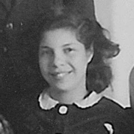 Vintage black and white photo of a young girl with curly hair, smiling, wearing a dark sailor-style outfit.