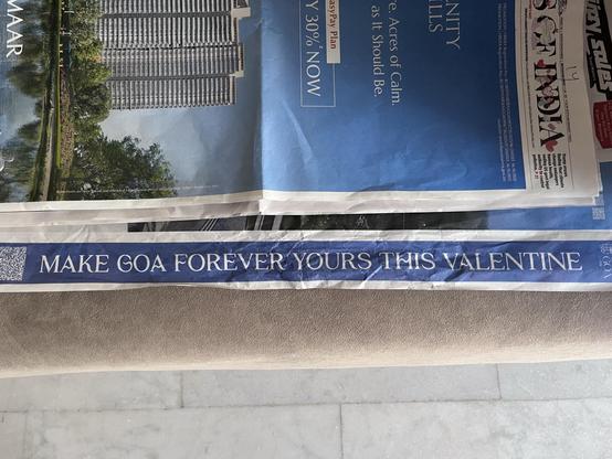 A close-up of a printed advertisement featuring the text "MAKE GOA FOREVER YOURS THIS VALENTINE" on a blue and white banner on the side of a newspaper.