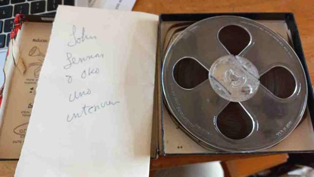 Photograph of a box containing an old 8mm(?) reel to reel tape and a hand written note "John Lennon Yoko Ono Amsterdam"