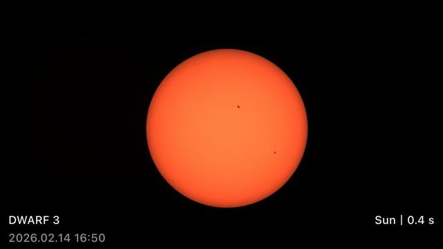 A bright orange Sun with two small dark spots on its surface, against a black background.