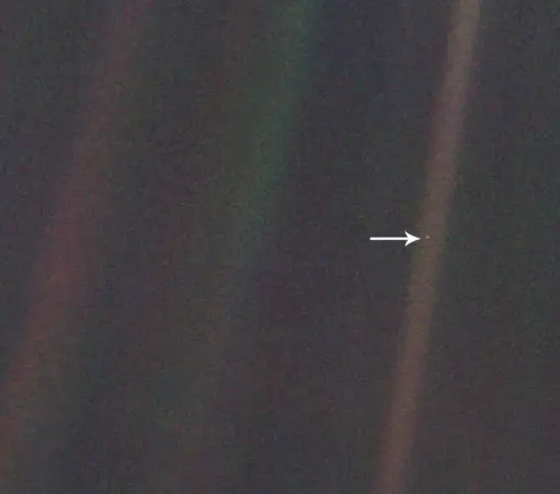 A grainy, low resolution image of space, with faint bright-colored streaks. An arrow points to a small dot, our very own planet Earth.
