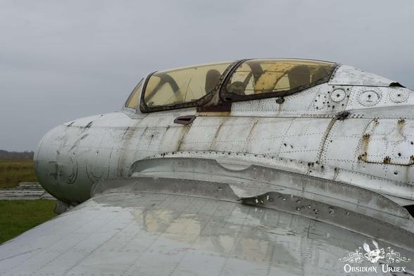 A weathered, riveted silver airplane under a cloudy sky, showing a yellowed cockpit canopy.