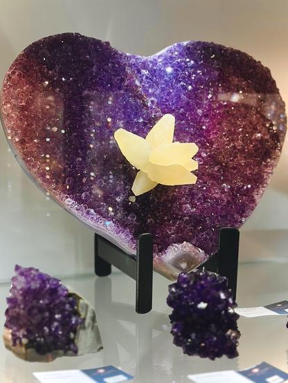 Half of a geode sliced and prepared very carefully to not dislodge the pale yellow calcite cluster of large crystals. The entire specimen is about 22” wide and the calcite is about 4” across with 8 petals as it looks like a flower cluster to me. The main crystals are reddish purple amethyst with some near the op more deep purple.