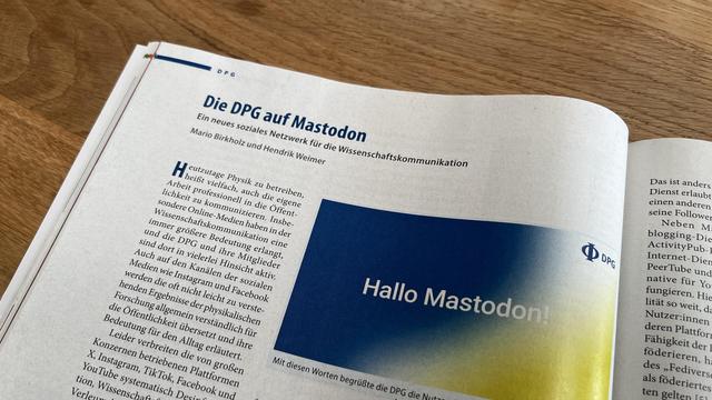Geöffnete Zeitschrift der DPG auf einem Holztisch, Titel des Artikels „Die DPG auf Mastodon“