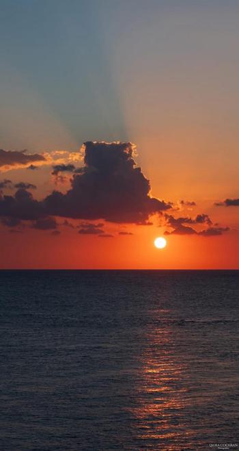 A sunset creates rays in the sky and is reflected in the sea.