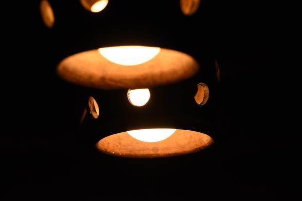 Bottom half of two hanging lamps. The outside and the inside of the lamps is visible.
 
The lamps are ceramic. The outside is dark brown, the inside is light brown. The bulbs are large and emit a soft yellow light. 

The lamps are shaped like a bell and there are small round openings that let the light out.