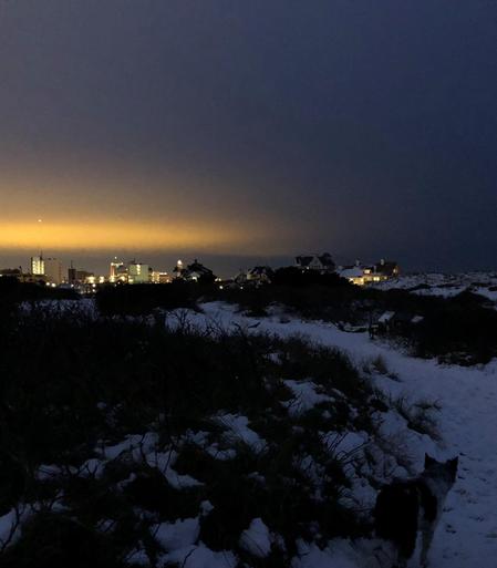 Blick aus dem verschneiten Dünengelände auf die erleuchtete Nacht in der Stadt