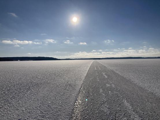 A view of lake Ekoln, looking South. The lake is all frozen, with a thin snow cover on the ice. It’s a cold but sunny day. It’s mostly quiet out here in the middle of the lake, but we can hear the ice creak and vibrate.