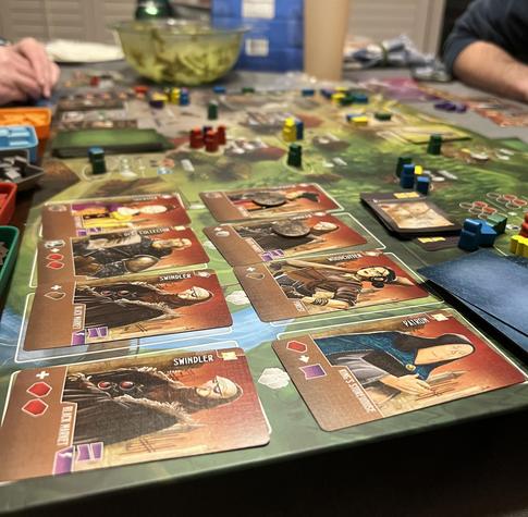 Photo of the game board with cards and pieces on a colourful green background.