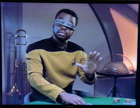 Photo of my TV. It’s Star Trek: The Next Generation. You see Geordi La Forge, chief engineer, holding his hand up like “no, wait” seated at a card table playing poker. 

This is the exact moment screenshotted and used in the “not this / but that” meme format.