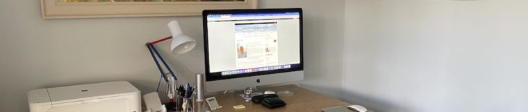 A photo of a neat and tidy desk with a desktop computer, lamp, iPad, keyboard, printer and stationery items on it.