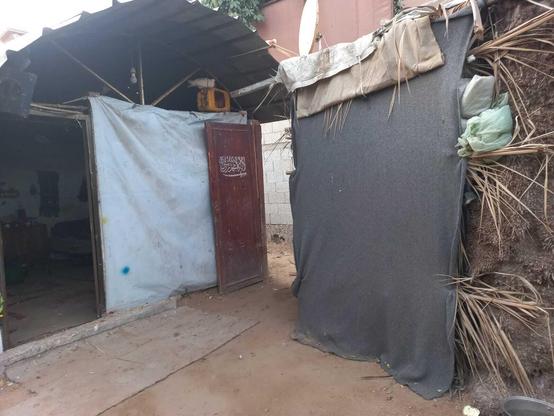 Makeshift shelters with tarp and cloth walls, a metal roof, and a wooden door with Arabic script.