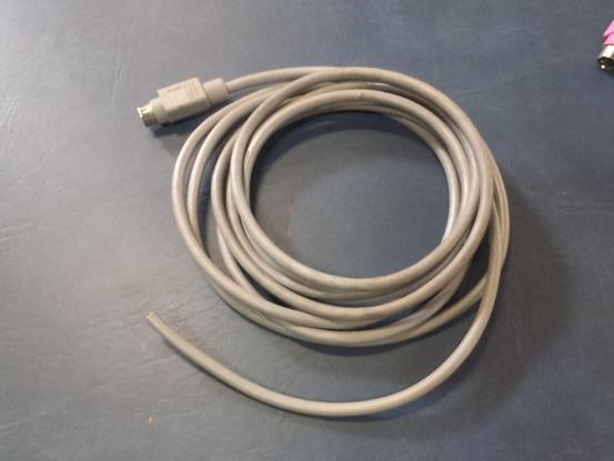 A gray cable coiled on a blue background. One end has been cut off and the other has a male mini-DIN connector without any logo or symbol on it.