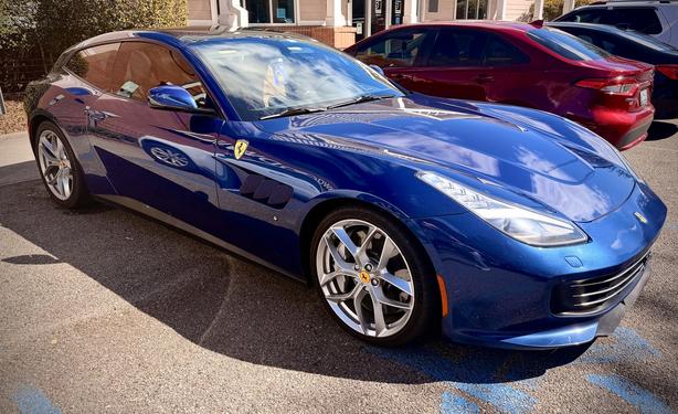 A beautiful blue Ferrari with a handicapped tag in handicapped parking outside a Goodwill.