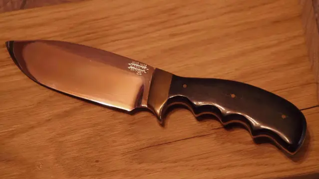 Messer mit sehr breiter Klinge auf einem Holzbrett. Der Griff ist aus dunklem Holz und das Heft aus Messing