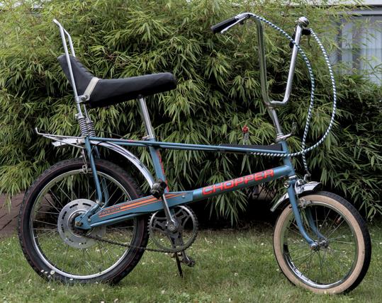 Ein Fahrrad mit einem 20" Hinterreifen, einem 16" Vorderreifen, einem geschwungenen Lenker und einem langen Sattel. Es ist blau und hat die leuchtend-orange Aufschrift "Chopper".