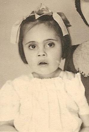Vintage black-and-white photo of a young girl with wide eyes, wearing a dress and bow in their hair.