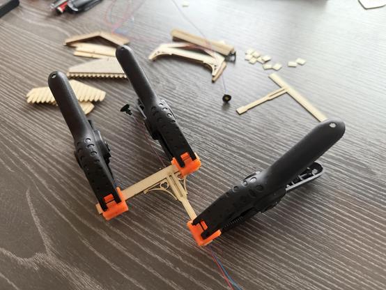 A close-up of three black clamps holding a canopy support while the glue holding the layers together sets. Behind it are assorted parts for the canopy framework.