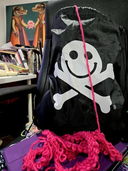 A DEF CON bag with bright pink yarn coming out of it, a mostly frogged disaster blanket