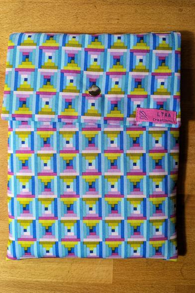 Rechthoekige stoffen hoes waar het klepje met een drukker is gesloten; de stof is veelkleurig en opgebouwd uit kleine staafjes die vierkantjes vormen.