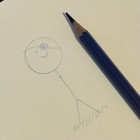 Muñeco palo sin brazos, pero con parche con lápiz azul sobre libreta. Es la base del personaje que vaya a tocar hoy en el juego.