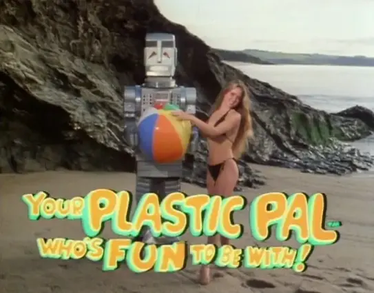 A woman in a bathing suit and bikini is holding a beach-ball while playfully standing beside a grim looking steel colored robot on a beach. The text "Your Plastic Pal Who's Fun To Be With!" is displayed in cartoonish letters beneath.