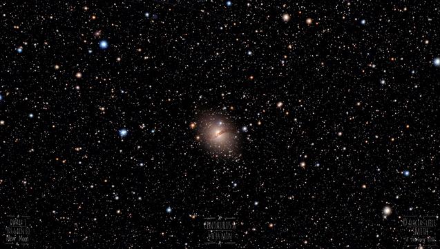 An unusual Galaxy with a dark stripe across it is in the centre of a well populated star field. There are distinctly red and blue tinted stars, and a faint satellite trail at the top of the image.